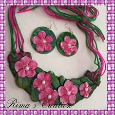 a necklace and earring set with pink flowers on green leaves in the shape of a circle