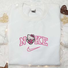 Introducing the Nike x Hello Kitty Angel With Pink Heart Embroidered Shirt, the perfect blend of sporty and cute. Made with high-quality materials, this shirt features a beautiful embroidery of Hello Kitty as an angel with a pink heart. Whether you’re hitting the gym or hanging out with friends, this shirt will make you stand [...] Cute Hoodie With Embroidered Graphics For Streetwear, Cute Hooded Tops With Embroidered Logo, Cute Hooded Top With Embroidered Logo, White Sporty Sweatshirt With Letter Embroidery, Sporty White Sweatshirt With Letter Embroidery, White Tops With Letter Embroidery For Sports Season, Cute Embroidered Logo Sweatshirt For Streetwear, White Sporty Hoodie With Letter Embroidery, Sporty White Hoodie With Letter Embroidery