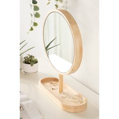 a round mirror sitting on top of a wooden stand next to a potted plant