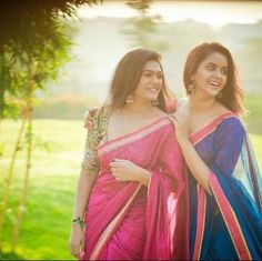 two beautiful women in sari standing next to each other on a lush green field