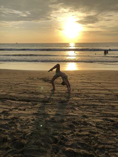 a person doing a handstand on the beach in front of the ocean at sunset