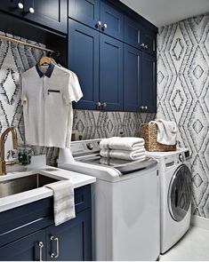 a washer and dryer in a laundry room with blue cabinets, patterned wallpaper