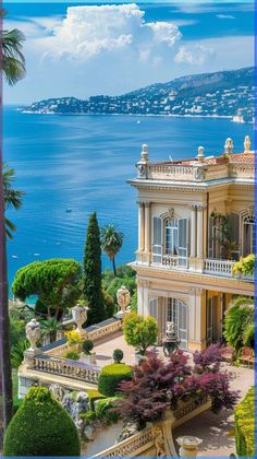 an ornate house overlooking the ocean with trees and bushes in front of it on a sunny day