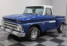 an old blue pickup truck is parked in a room with black and white checkered flooring