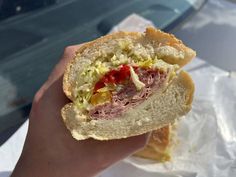 a hand holding a half eaten sandwich with meat and lettuce on it's side