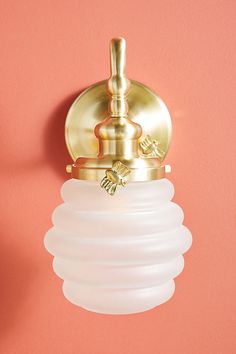 a wall light with a white glass shade hanging from it's side on a pink wall