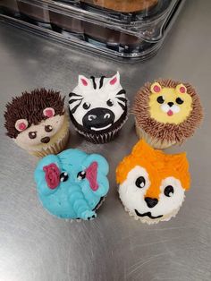 four cupcakes with different designs on them sitting on a metal surface next to a plastic container