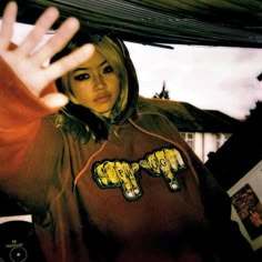 a woman in a brown hoodie holding her hand up