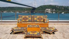 a couch and ottoman sitting on top of a wooden floor next to the ocean with a bridge in the background