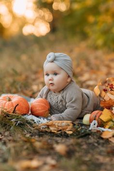 a baby sitting on the ground next to pumpkins