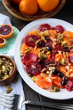 a white plate topped with oranges and nuts next to a bowl of dried fruit