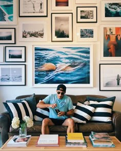 a man sitting on top of a couch in front of a wall covered with pictures