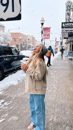 a woman standing in the snow next to a street sign