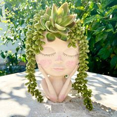 a ceramic head with plants growing out of it's face on top of a rock