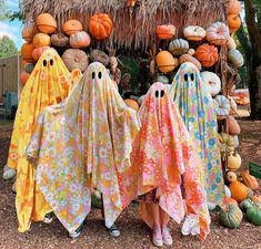 three people dressed up as ghost in front of pumpkins