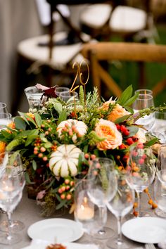 an arrangement of flowers and candles on a table with wine glasses, plates and utensils