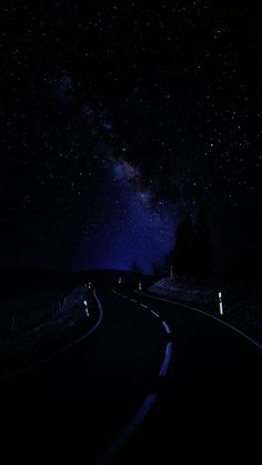 the night sky is filled with stars above a winding road