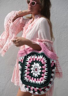 a woman is holding a crocheted bag in front of her face and wearing sunglasses