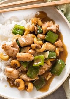 a white plate topped with chicken and vegetables next to chopsticks on top of rice