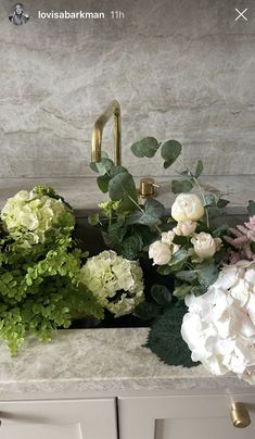 white flowers and greenery are sitting on the counter top in front of a faucet