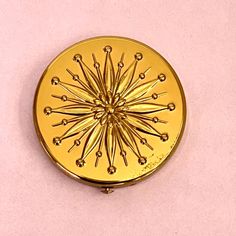 a gold colored compact case sitting on top of a pink surface with pins in it