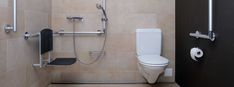 a bathroom with a toilet, shower head and handrails in beige tile walls