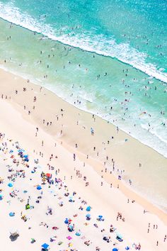 an aerial view of people on the beach and in the water with blue umbrellas