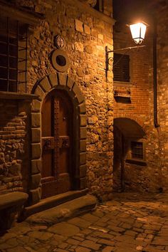 an alleyway with stone buildings and cobblestone streets at night, lit by street lamps