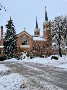 a church with two steeples and trees in the front is covered in snow on a winter day