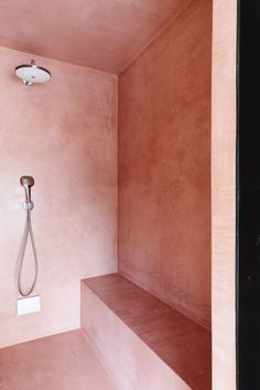 a bathroom with pink walls and a shower head in the corner next to a bench