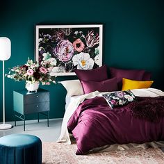 a bedroom with teal walls, purple bedding and floral artwork on the wall