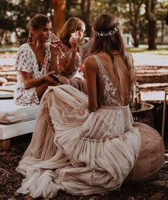 two women in dresses sitting on the ground with one woman looking at her cell phone