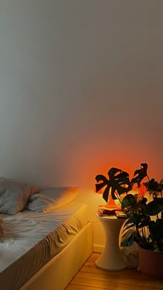 a bed with white sheets and pillows next to a potted plant on the floor