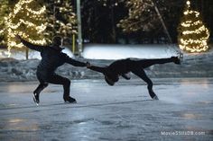 two people are skating on an ice rink at night with christmas lights in the background