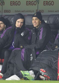 two soccer players sitting next to each other in the dugout during a game,