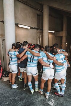 a group of rugby players huddle together in an indoor area with columns and concrete walls