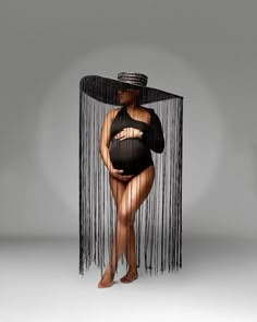 a woman in a black dress and hat standing behind a sheer curtain with her belly exposed