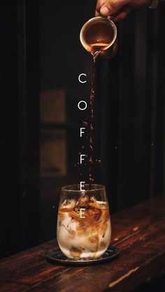 someone pouring coffee into a glass on top of a wooden table