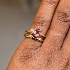 a woman's hand with two gold rings and a pink diamond ring on it