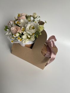 a bouquet of flowers in a brown box on a white surface with a pink ribbon