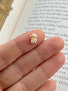 a tiny white teddy bear sitting on top of a persons finger in front of an open book