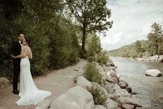 a bride and groom standing next to the river