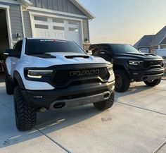 two black and white dodge trucks parked in front of a house with garage doors open