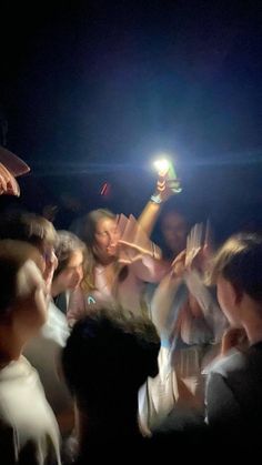 a group of people standing around each other holding up cell phones in the air with their hands