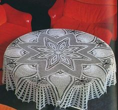 an old crocheted doily table with red chairs in the backgroud