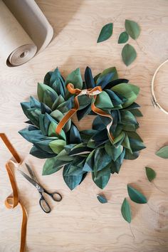 a wreath with leaves and scissors on a table next to some ribbon, tape and other crafting supplies