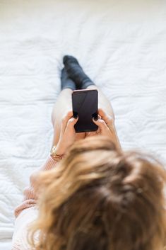 a woman laying on top of a bed holding a smart phone