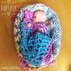 a baby doll in a crocheted basket with a pink teddy bear on it