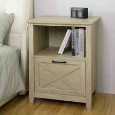 a night stand with books on it next to a bed in a room that has white walls and wood floors