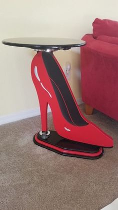 a red high heeled table with a glass top and black base on the floor